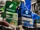 Editorial collage showing Robinhood, Coinbase and Gemini on uneven stacks of financial papers, symbolizing differences in event-contract revenue.